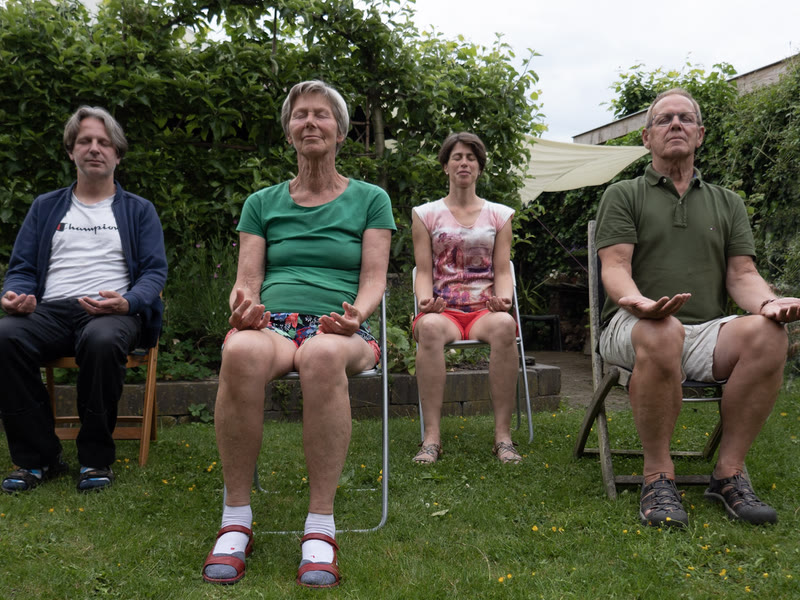 Vier deelnemers mediteren met de ogen dicht op een stoel